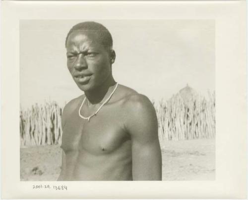 Man standing, with a kraal fence in the background (print is a cropped image)