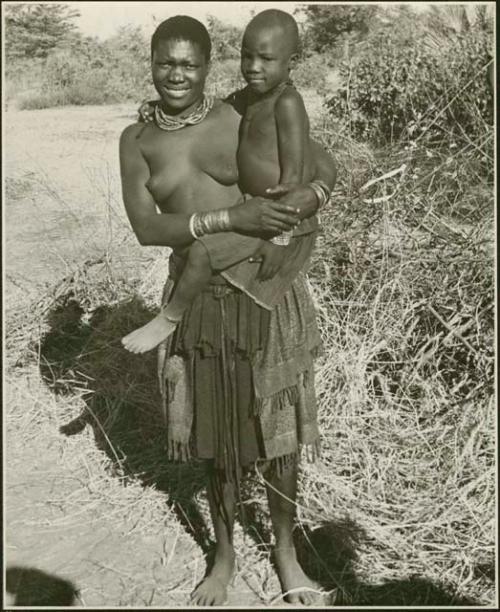 Woman standing and holding a child (print is a cropped image)