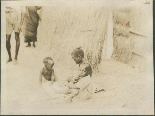 Three children sitting outside hut, village near the Nile River