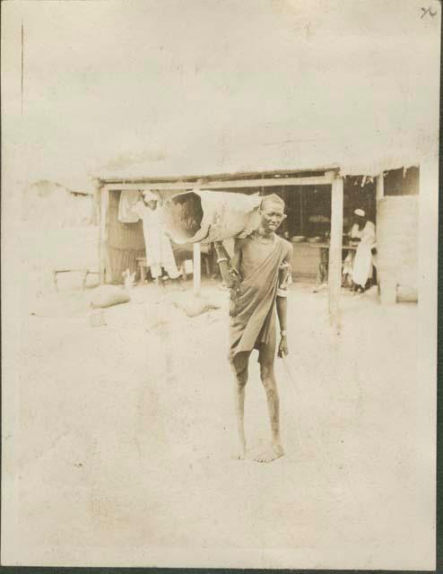 Man carrying unknown object posing for photograph, village near Nile River