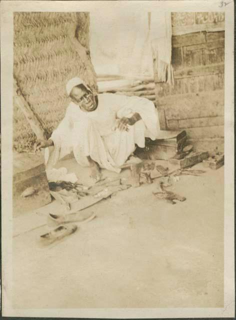 Man in white dress sitting under hut canopy in Malakal, a British post