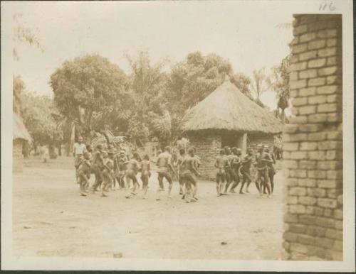 Pygmies dancing, with view of bricked building in background