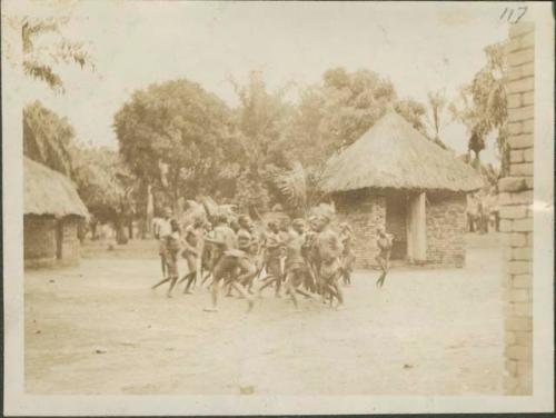 Pygmies dancing, with view of bricked building in background