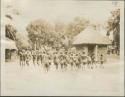 Pygmies dancing, with view of bricked building in background