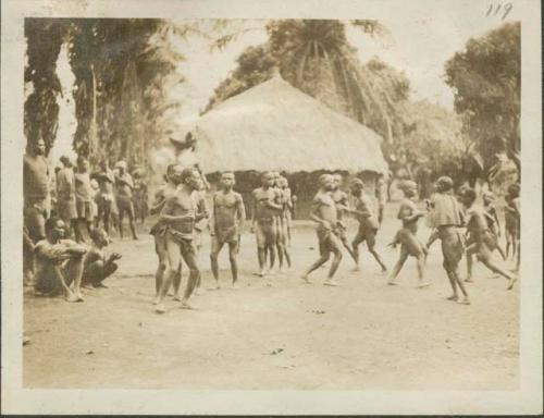 Pygmies dancing, with view of bricked building in background