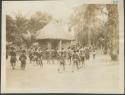 Pygmies dancing, with view of bricked building in background