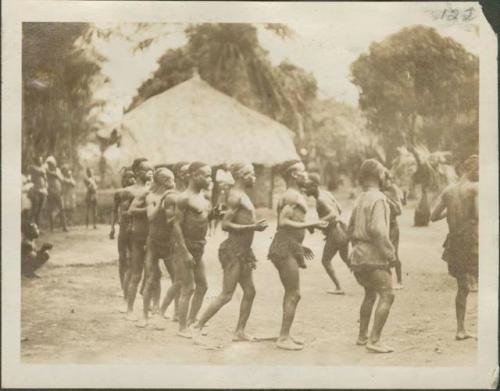 Pygmies dancing, with view of bricked building in background