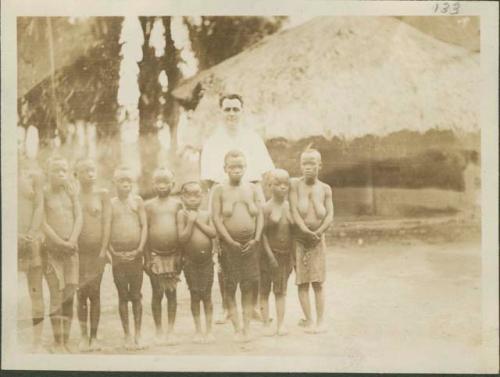 Pygmy women and young girls posing for photograph before non-Pygmy man in white shirt