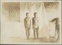 Two Pygmy men posing for photograph before curtain, frontal view