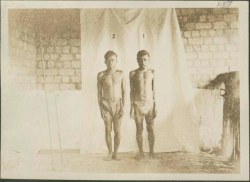 Two Pygmy men posing for photograph before curtain, frontal view