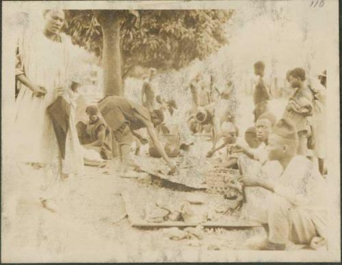 Crowd on main street of village, those in fez hats and whote robes are Muslims from further north