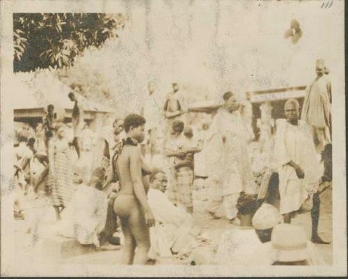 Crowd on main street of village, those in fez hats and whote robes are Muslims from further north