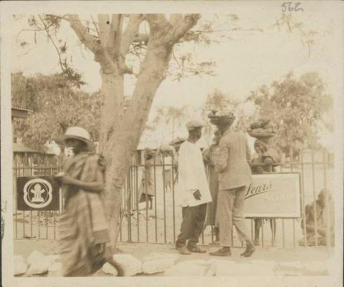 People talking over a metal fence with sign for Sears soap