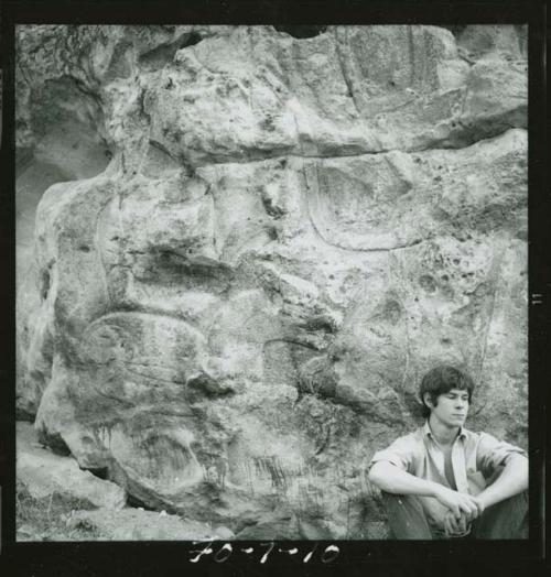 Man sitting in front of rock formation (monument?) with sculpture