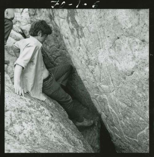 Man sitting on rock looking at petroglyph on rock facing him.