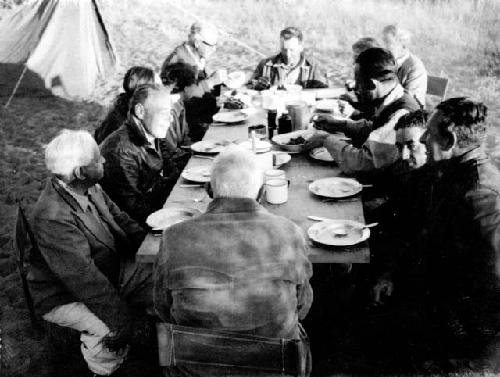 Group of expedition members and other people sitting around a large table, eating