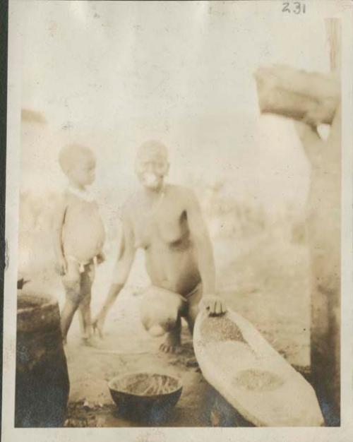 Woman grinding grain, child next to her