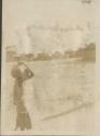 Person carrying jar, huts in background