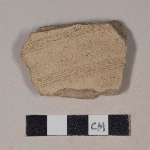 Coarse buff bodied earthenware body sherd, with buff slip and incised lines, burned interior