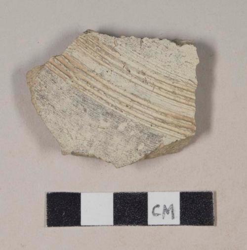 Coarse buff bodied earthenware body sherd, with buff and black slip and incised lines