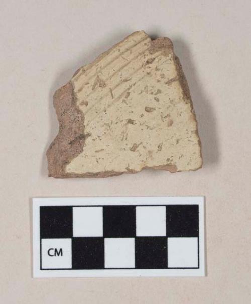 Coarse red bodied earthenware body sherd, with buff slip and incised lines