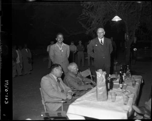 Group of people standing behind expedition members sitting at a table