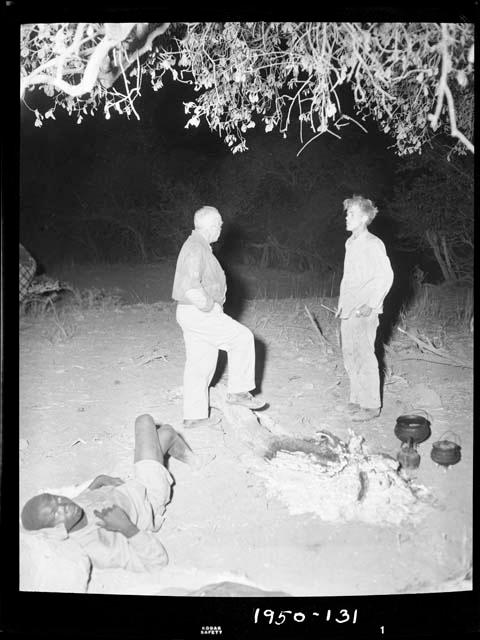 Man reclining next to Laurence Marshall and John Marshall standing in the expedition camp