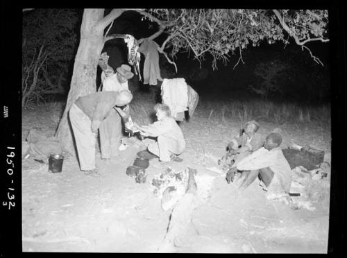 Expedition members sitting and standing in camp, including Edward Hartley, Laurence Marshall and John Marshall, with meat hanging in a tree behind them