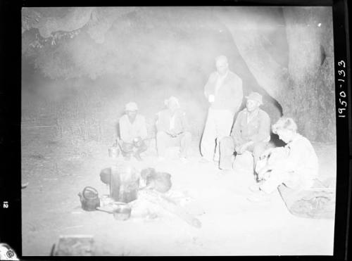 Expedition members sitting and standing around a cooking fire, including Edward Hartley, Laurence Marshall and John Marshall