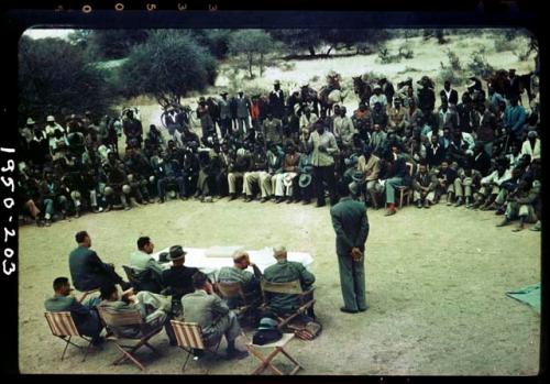 Indaba at Omajetti, Herero chief, with a large group of people sitting and standing behind him, addressing expedition members, including Colonel Hoogenhout, John Neser, Laurence Marshall and John Marshall