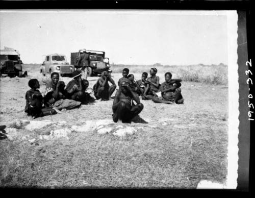 Group of people sitting, the first group that the expedition encountered, with expedition trucks in the background