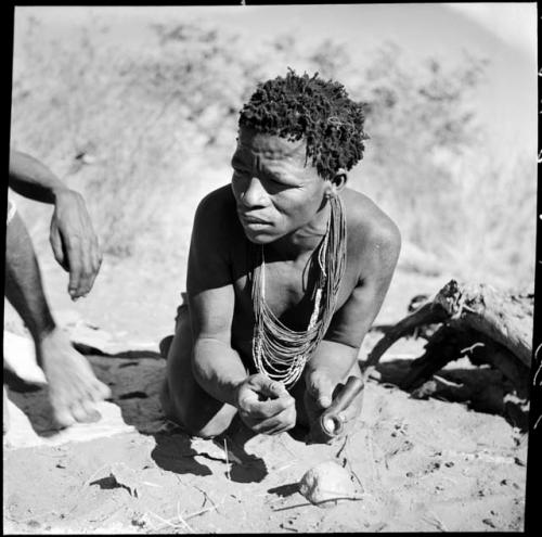 ≠Toma crouching and holding a soapstone pipe