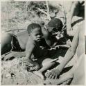 Child holding a large knife, sitting next to a man lying down