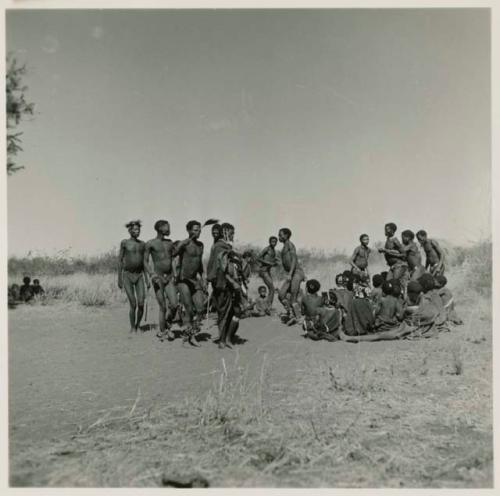 Group of men performing a curing dance around seated women, including /Gam and a medicine man holding another who is in trance