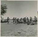 Group of men performing a curing dance, including /Gam dancing in the middle and a young man dancing behind her