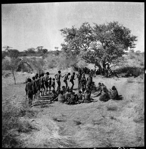 Men and one woman dancing around a circle of women sitting in an early stage of a daytime dance