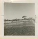 Person walking on wet ground, with a child standing with an expedition member watching them, distant view