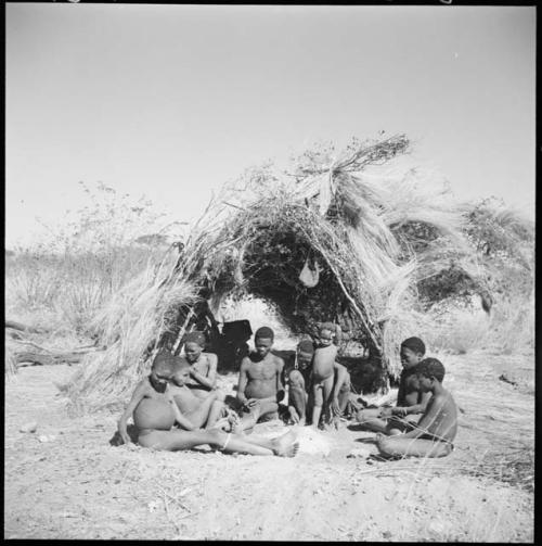 Gau of Band 2 sitting with his family in front of a skerm, including his son ≠Toma (by his first wife), his son !Naishi, Be (his first wife), Gau, Khuan//a (his second wife) and their son /Qui, /Gunda (Khuan//a's son by a first husband), and ≠Gao (son of Be and Gau)