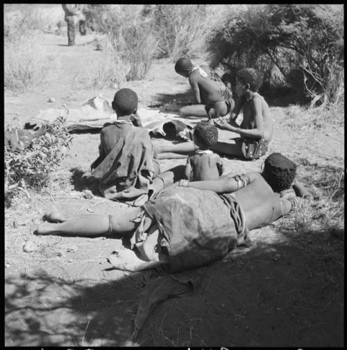 Group of people sitting, with a man scraping a hide, women watching him