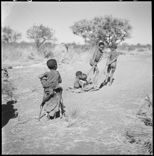 Tsamgao (≠Toma's son) and an unidentified boy pulling two babies on a kaross, with Be watching