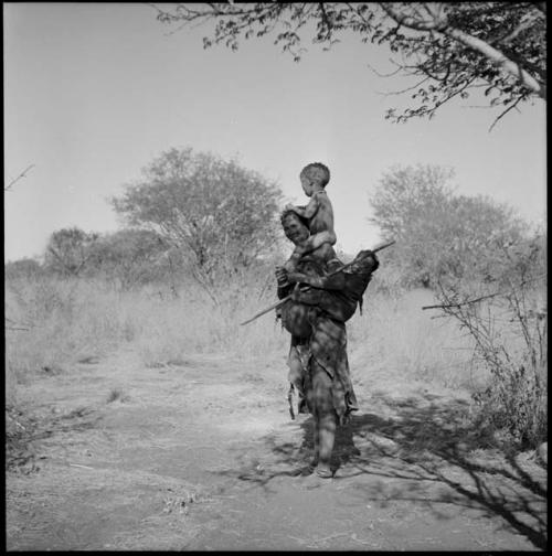 /Naoka (wife of /Ti!kay) carrying her son !Nani on her shoulders and her daughter /Khoa in her kaross