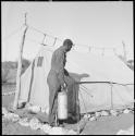 Expedition staff member spraying DDT beside a tent