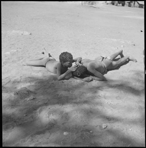 Boy and man lying on the ground, the boy is looking for lice in the man's hair