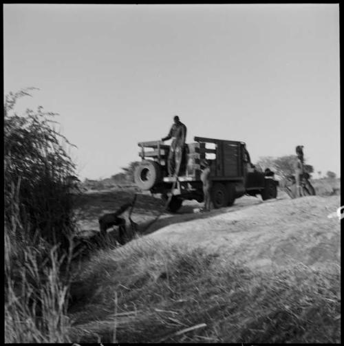 People watching expedition members pump water from a waterhole into the back of an expedition truck