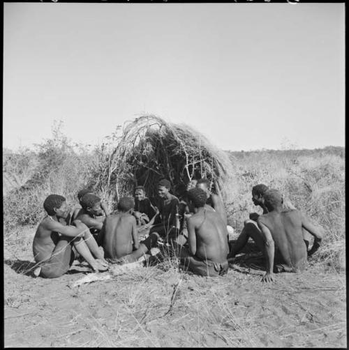 Group of people sitting in front of a skerm and telling stories, including Zuma (daughter of "Old Xama," wife of Gao), Gao (son of Debe, headman of Band 24 in Cho/ama), and /Qui (brother of "Gao Helmet")