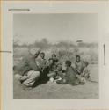 Group of people sitting, including Gau, "Old ≠Toma," /Gam and //Khuga (wife of !Naishi), with Laurence Marshall crouched next to them