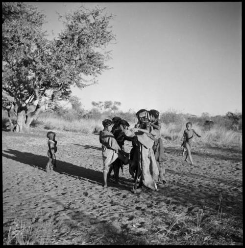 Girls playing N≠a N≠a Hau / N!hau-N!hau (the basket game), weaving their feet together and hopping around in a circle on one foot, singing