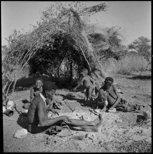 Gao of Band 2 sitting by his fire with his two wives, Be (behind him) and Khuan//a (right); Khuan//a is cracking a tsi nut