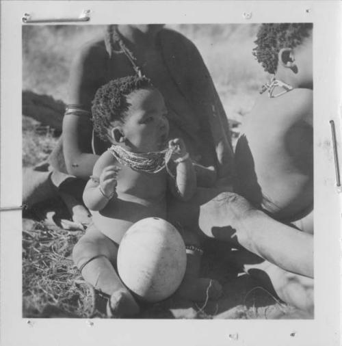 Baby (child of ≠Gao, leader of Band 10, and Bau, his first wife) sitting next to an ostrich eggshell