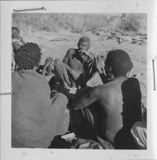 "Old Demi" holding his hand across his mouth, sitting with a group of people